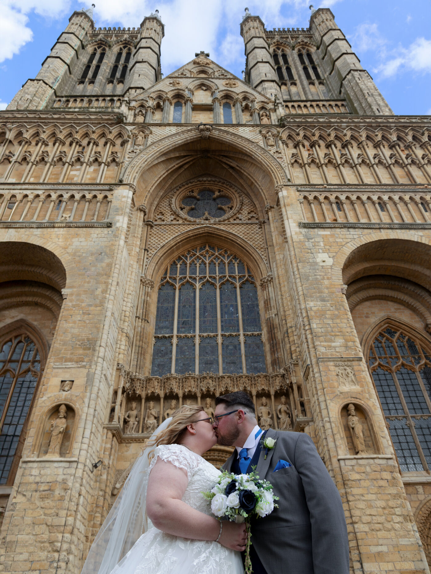 bride and groom kissing. stood in front of Lincoln cathedral. shot from below looking up