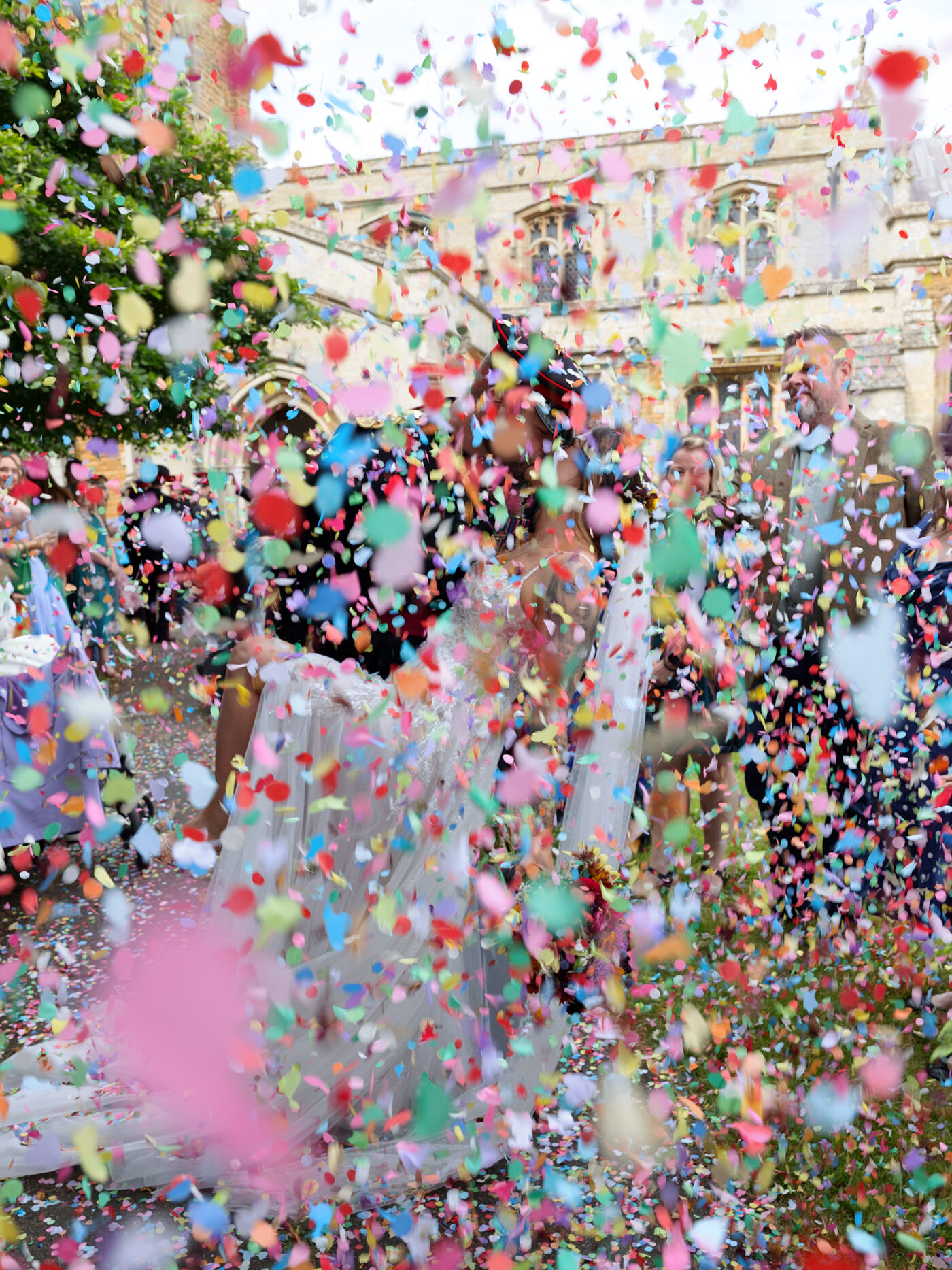 big storm of colourful confetti. Groom in army uniform dips his bride for a kiss.