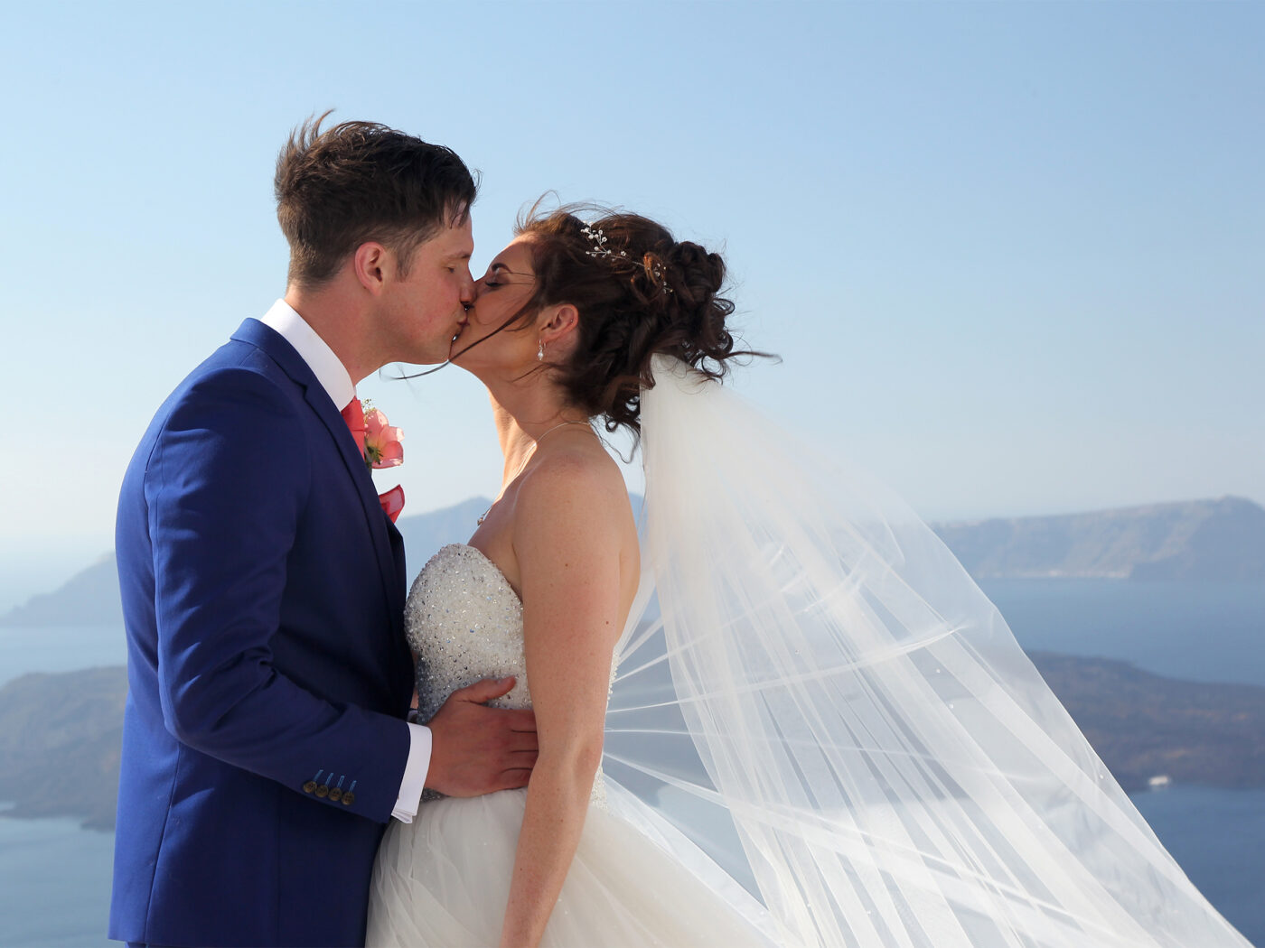 Bride and groom kissing. the brides veil is blowing in the santorini breeze