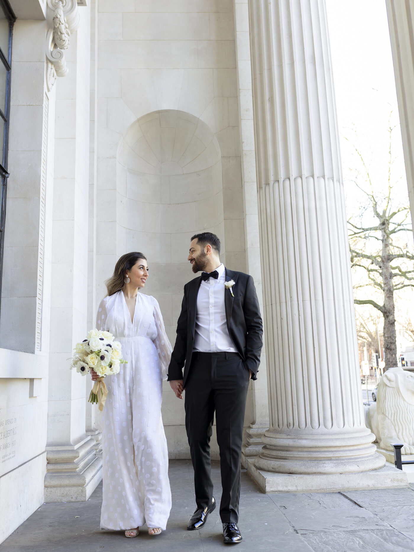 Bride and groom looking at each other stood outside the pillars of Marylebone town hall