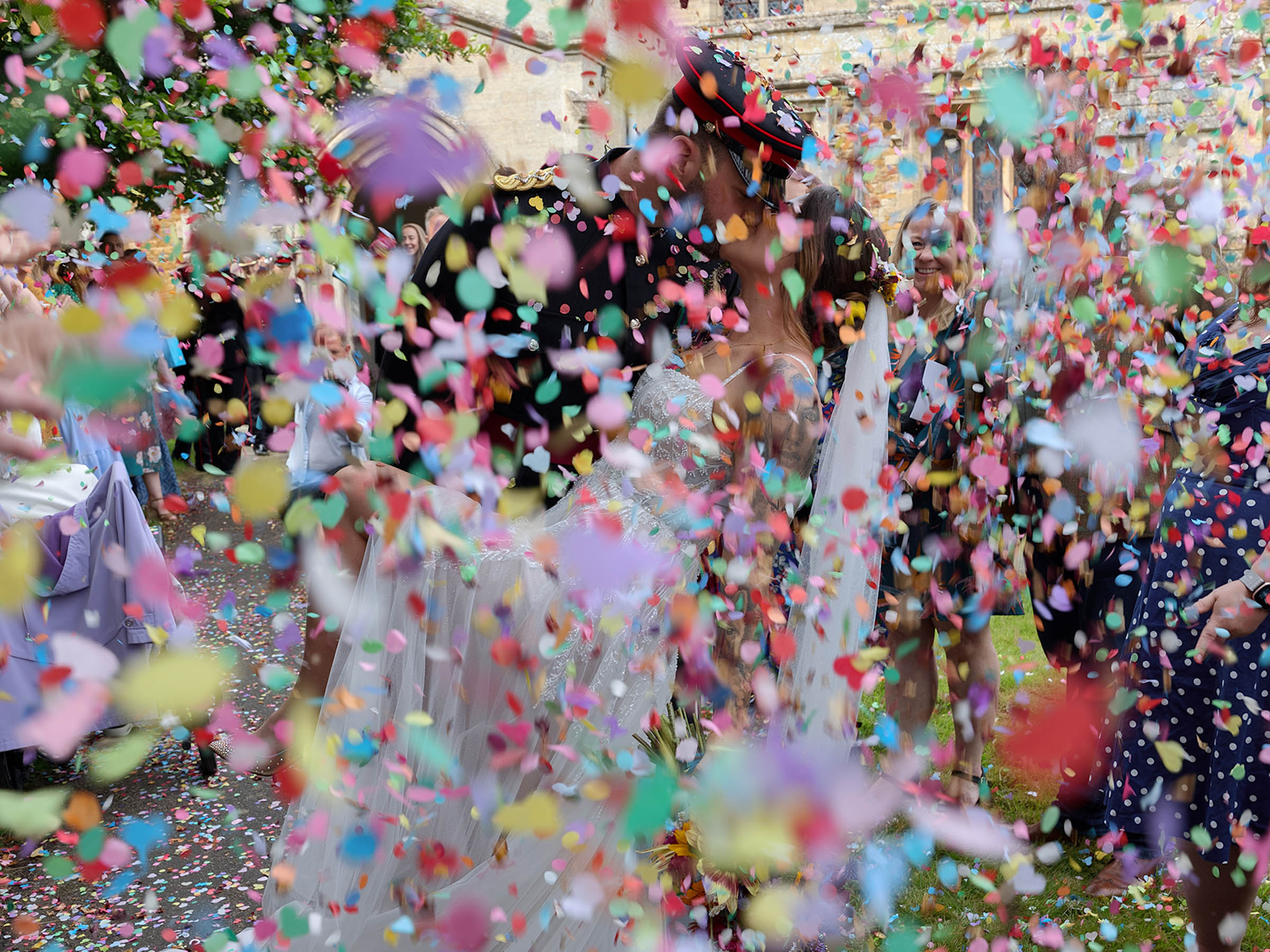 Bride and Groom kissing outside a church hidden by a mass of brightly coloured confetti