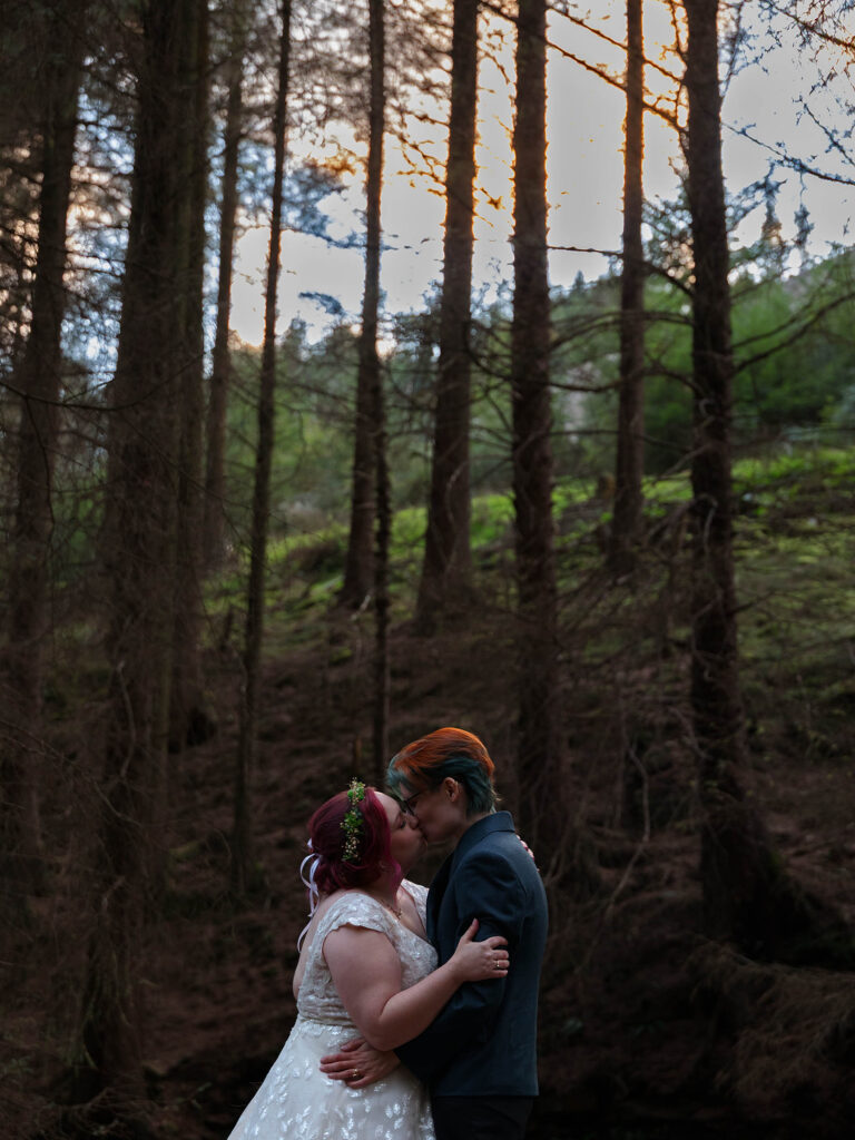 A newly wed couple embracing in a forest having a kiss.