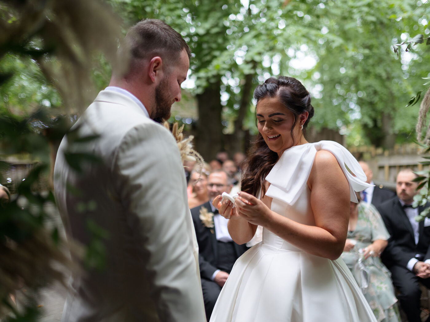 A Bride and Groom are mid wedding ceremony. they are smiling and the bride is looking at the tissue in her ands that she has just wiped her tears with. The wedding is at Alnwick Tree House