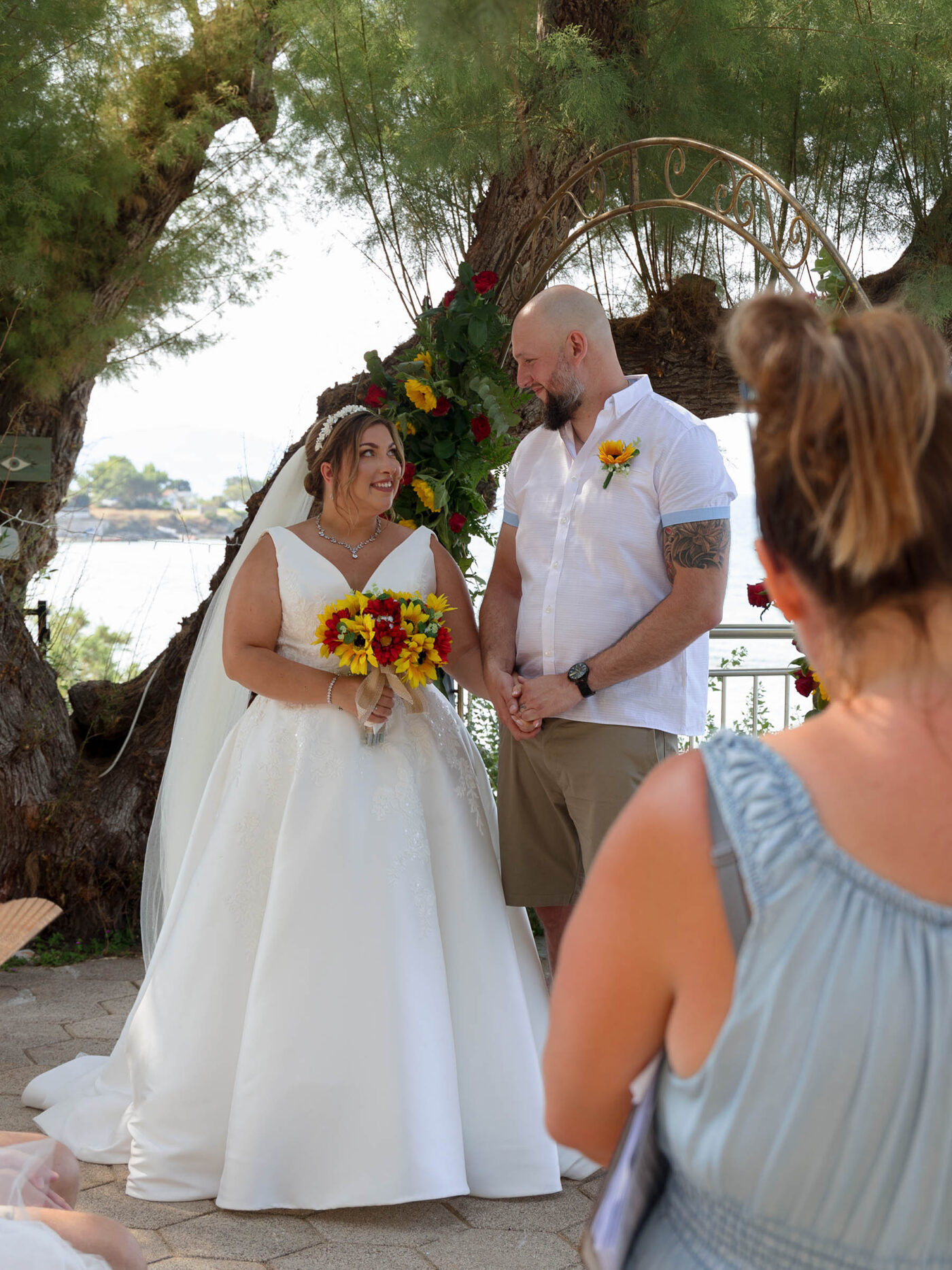 A Bride and Groom at their destination wedding in Zante stand next to each other holding hands. The sea is behind them and there are clifftop views