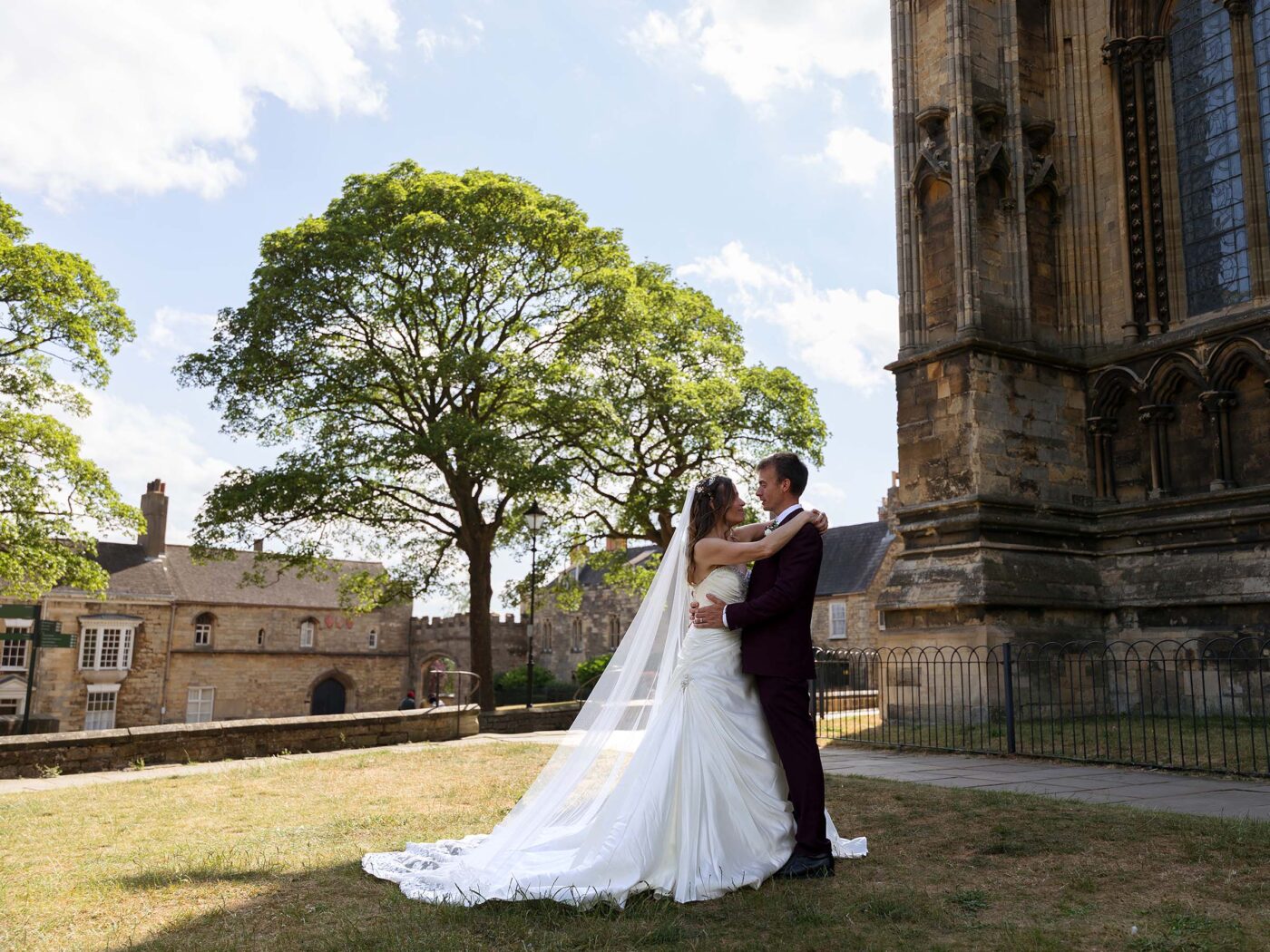 A bride and groom are hugging in the grounds of Lincoln Cathederal