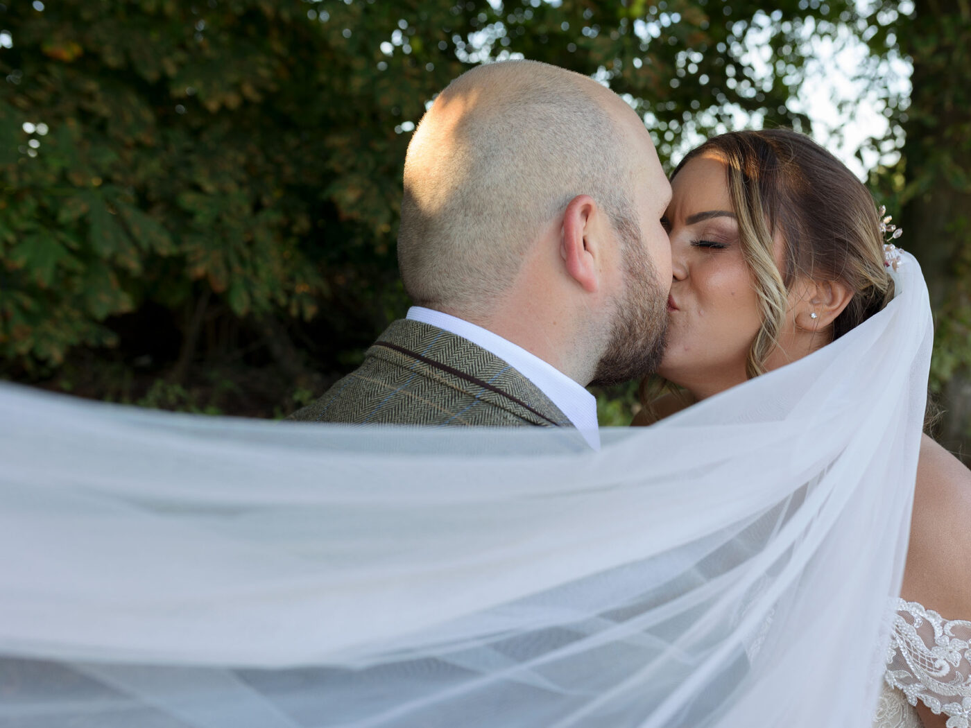 A couple kiss. The Brides veil swoops around them and across the frame