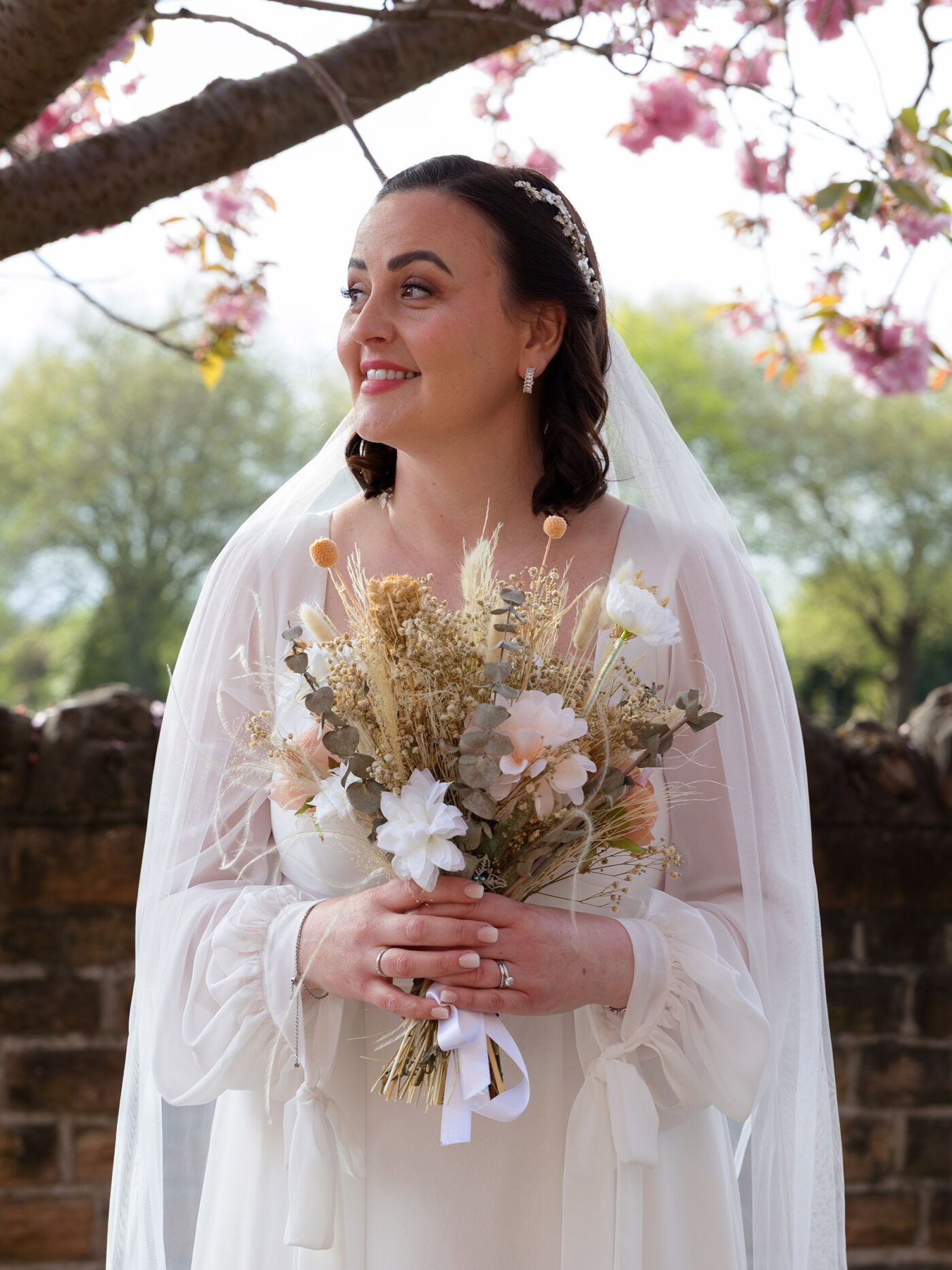 A radient Bride stands under a blossom tree looking to the distance
