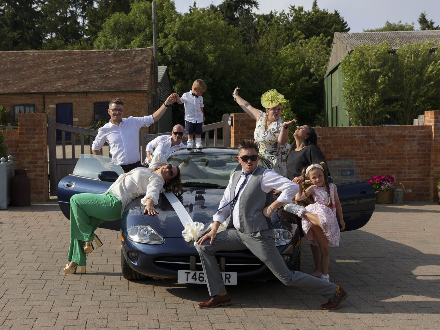 A different approch to wedding group sots. A group of people are stood in difefrent poses around and on a wedding car