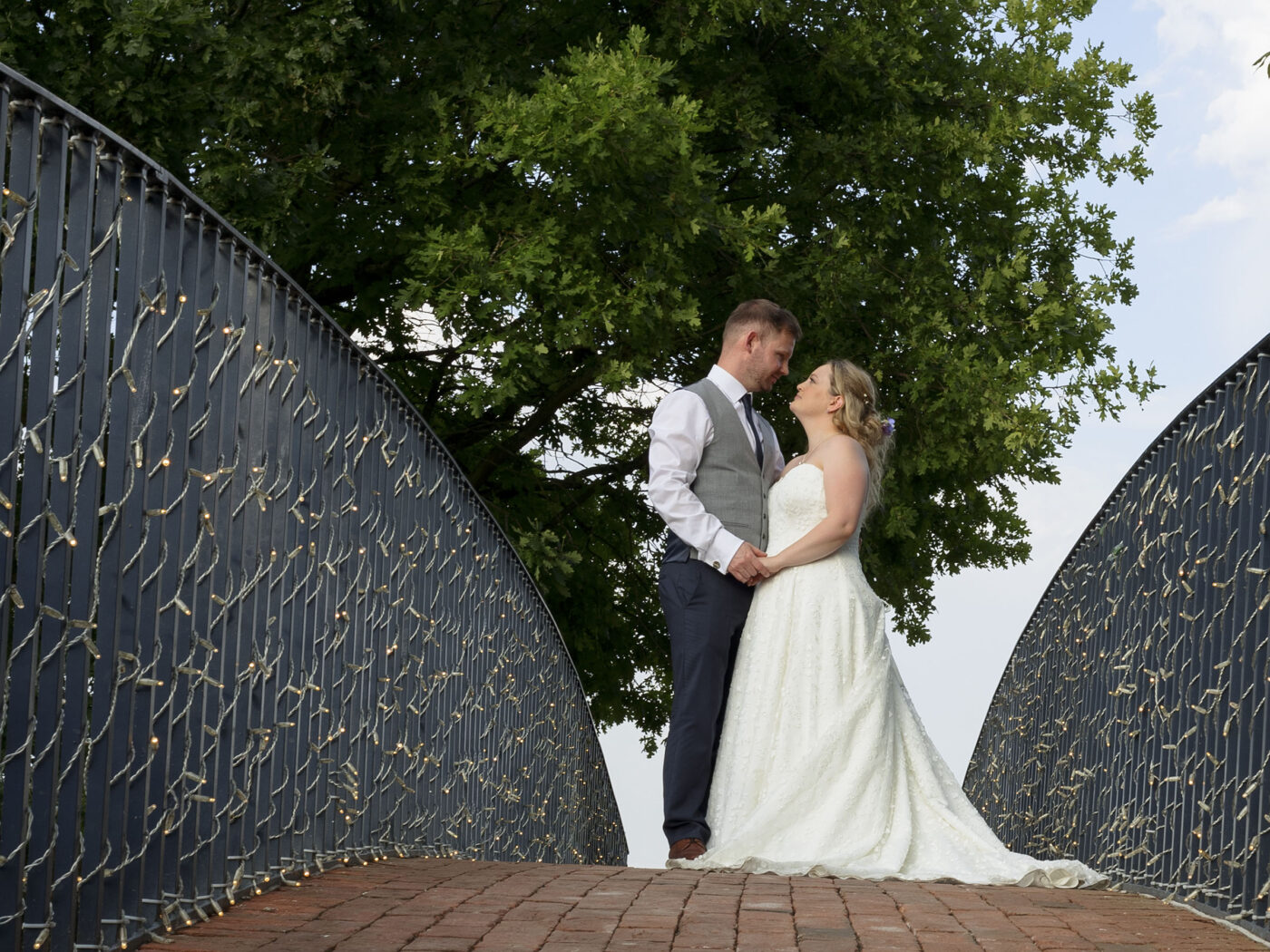 A Bride and groom are stood facing each other on an ornate bride at Bassmead Manor Barns