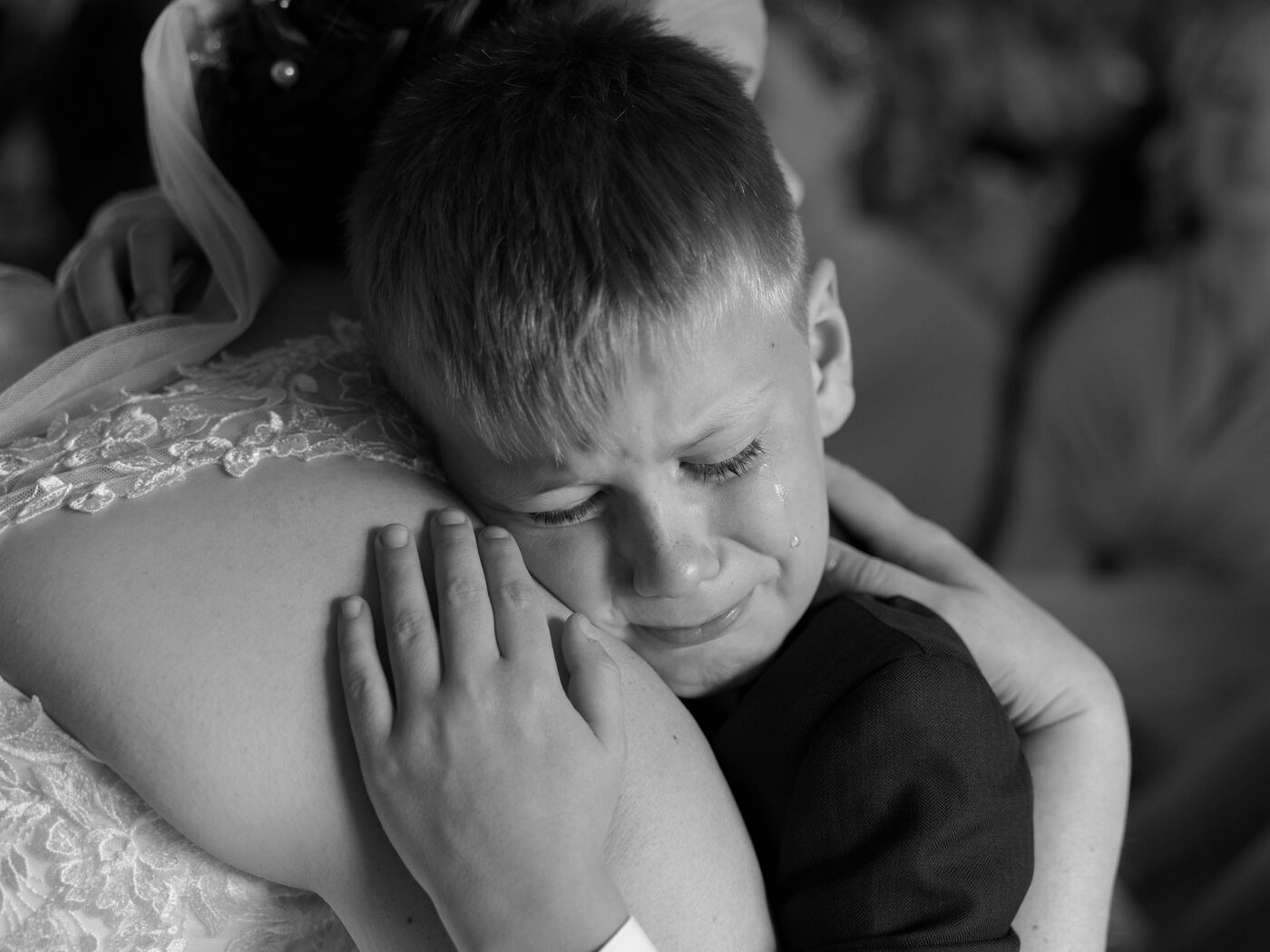 A young boy cries as he is comforted by his mum who is wearing a wedding dress