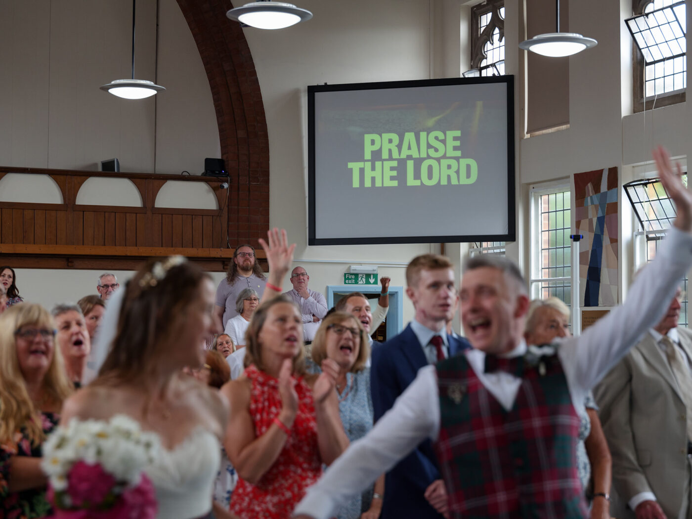 A bride and groom sing and celebrate their marriage witha big scren in the background with the words 