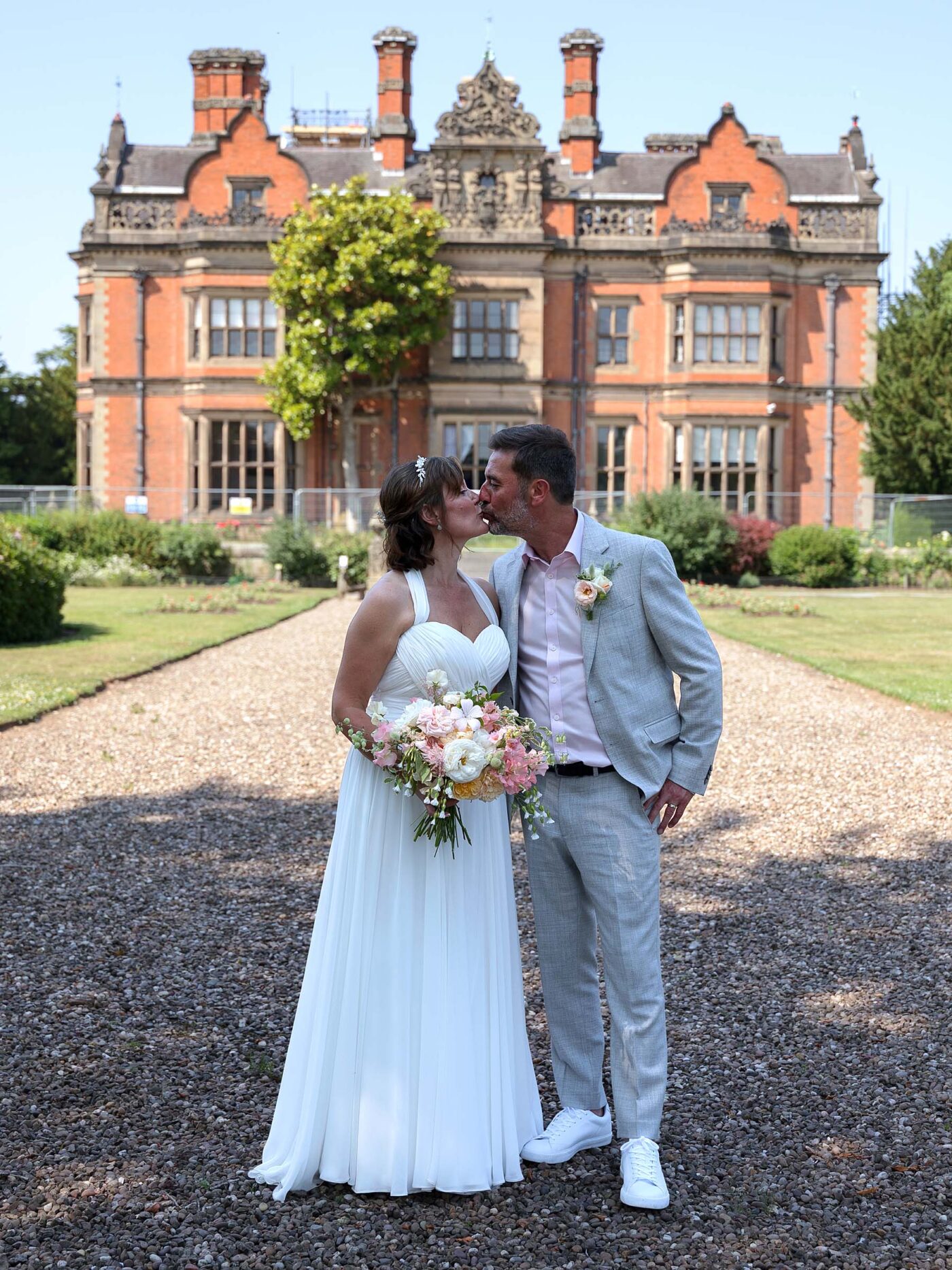 A Bride and Groom in relaxed wedding attire stand inf ront of Beaumanor Hall kissing