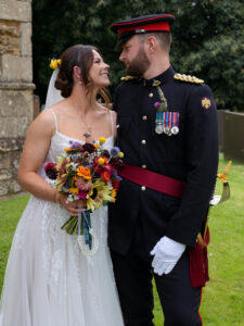 Groom wearing Army Uniform stands next to his Bride looking into each others eyes. They ares tood outside Harlaxton Church