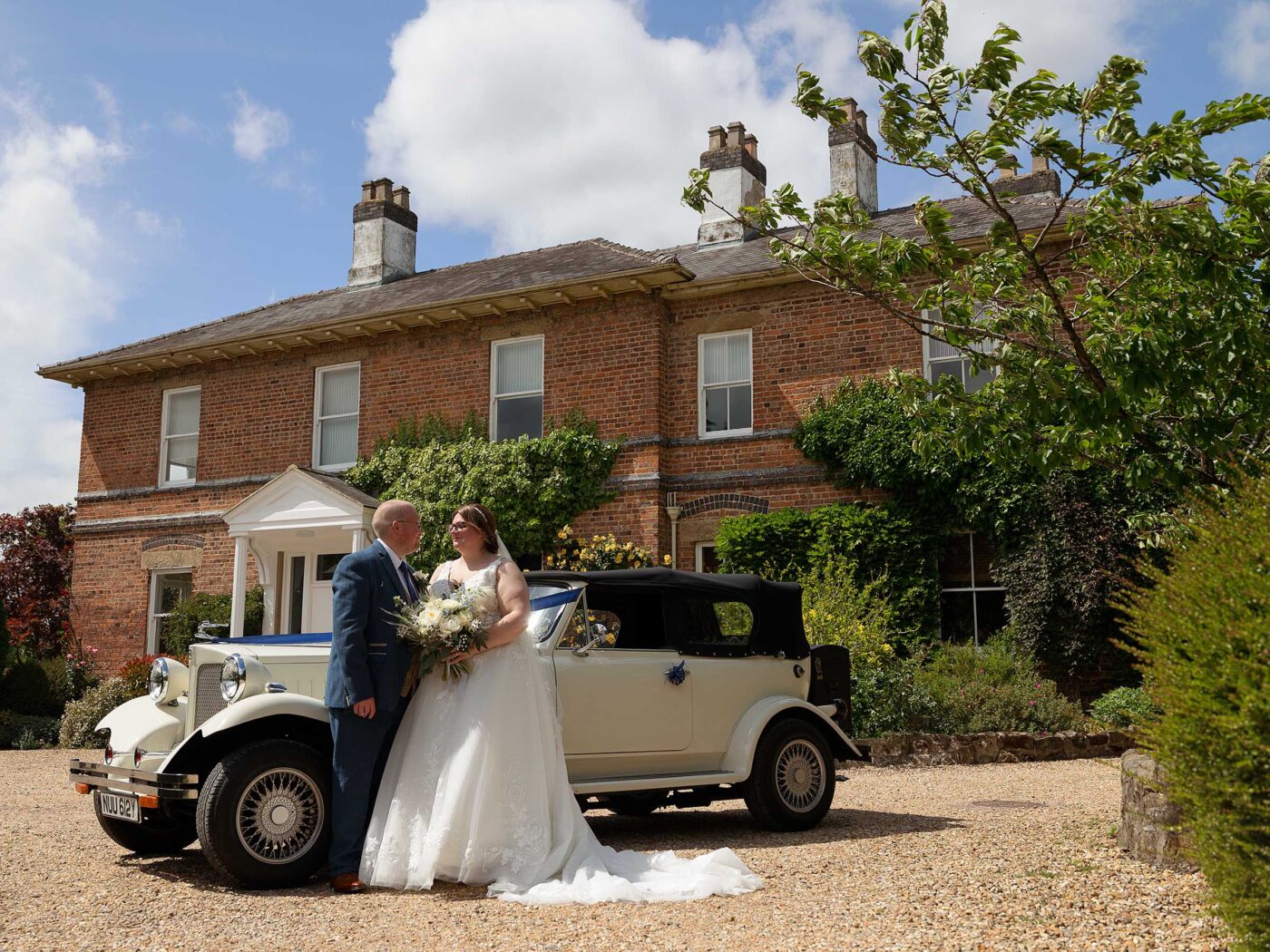 Bride and Groom stand next to their wedding car in front of Shottle Hall
