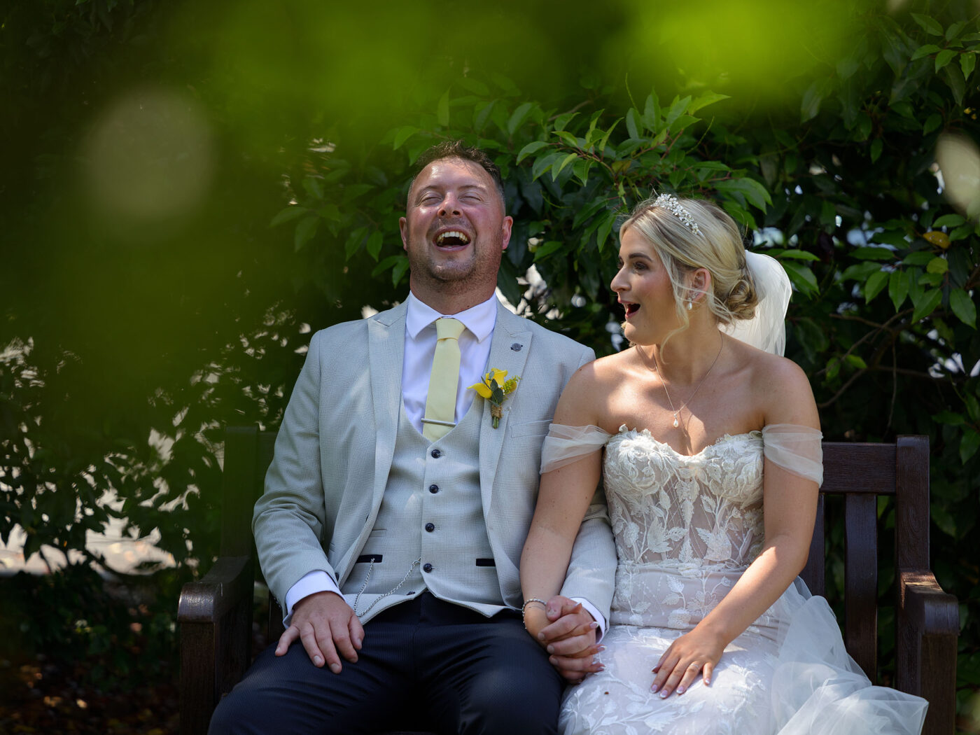 A Bride and Groom sit on a bench at Barnsdale sharing a joke and laughing
