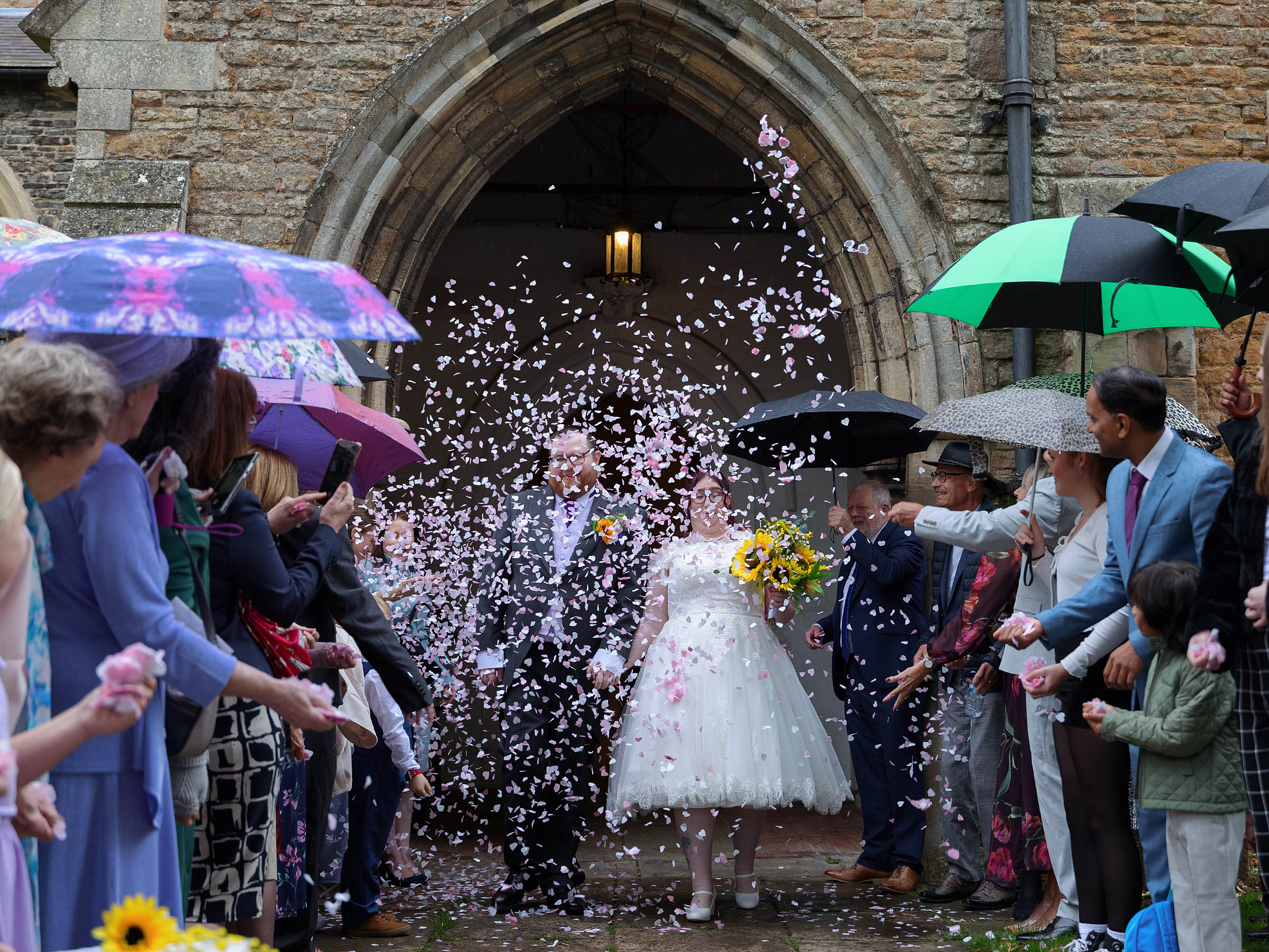 Bride and Groom kissing outside a church hidden by a mass of brightly coloured confetti