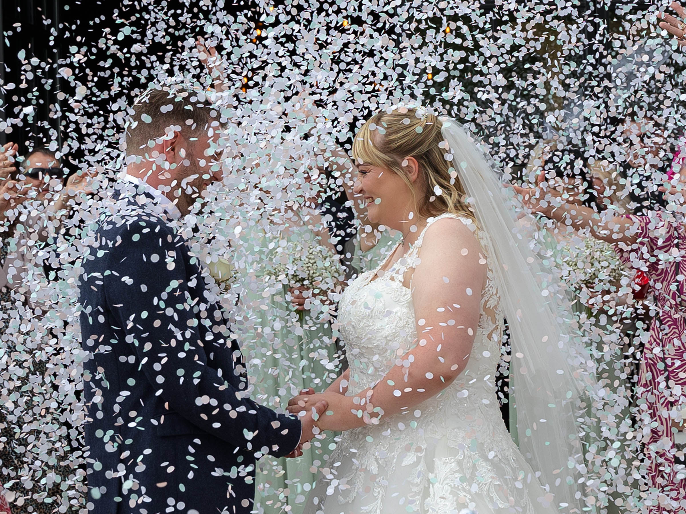 Raves and Reviews. A Bride and Groom facing each other hlding hands being showered with a huge amount of white confetti. Looks like a wedding snow storm. The photo accompanies a lovely review of Pink Photographics