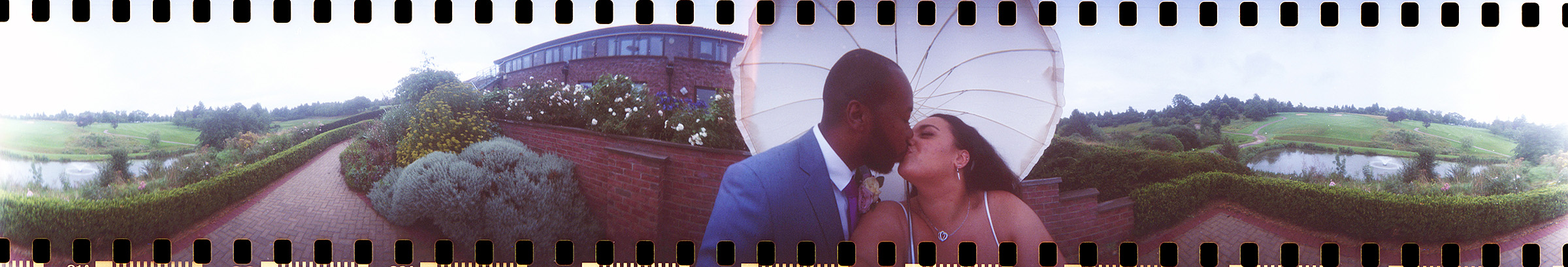 Filmstrip-style panoramic image of a couple kissing beneath a large white umbrella in a scenic outdoor setting.This is part of Pink Photographics portfolio page