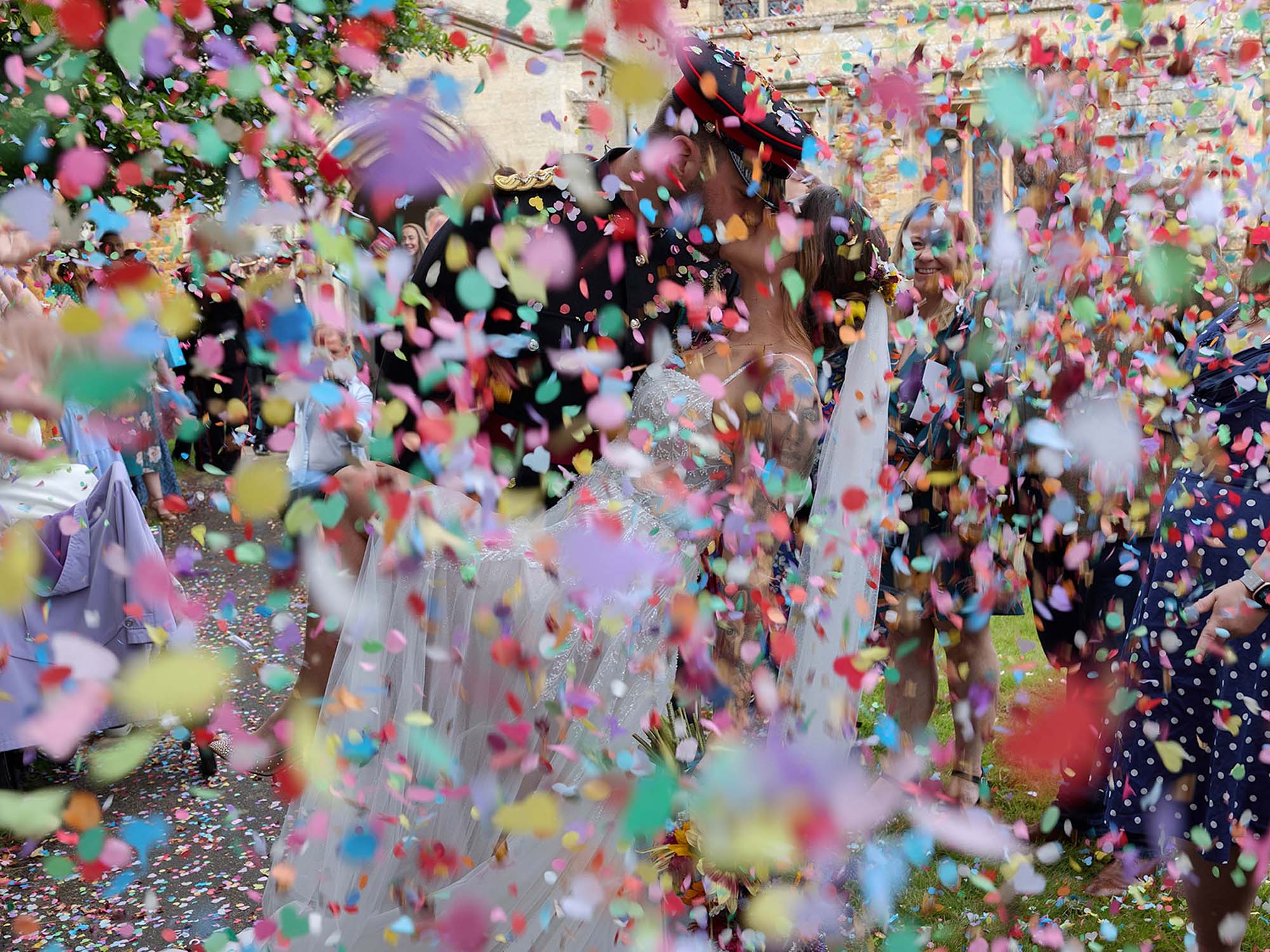 A joyful outdoor confetti moment with guests celebrating as the couple stand together beneath a shower of colourful paper.