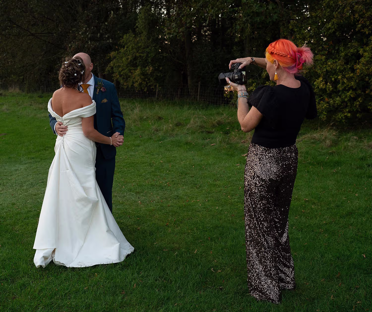 Lincolnshire Wedding Photographer Pink Photographics, a photographer with bright pink hair photographs a bride and groom embracing on a grassy lawn at dusk at Scrivelsby Walled Gardens